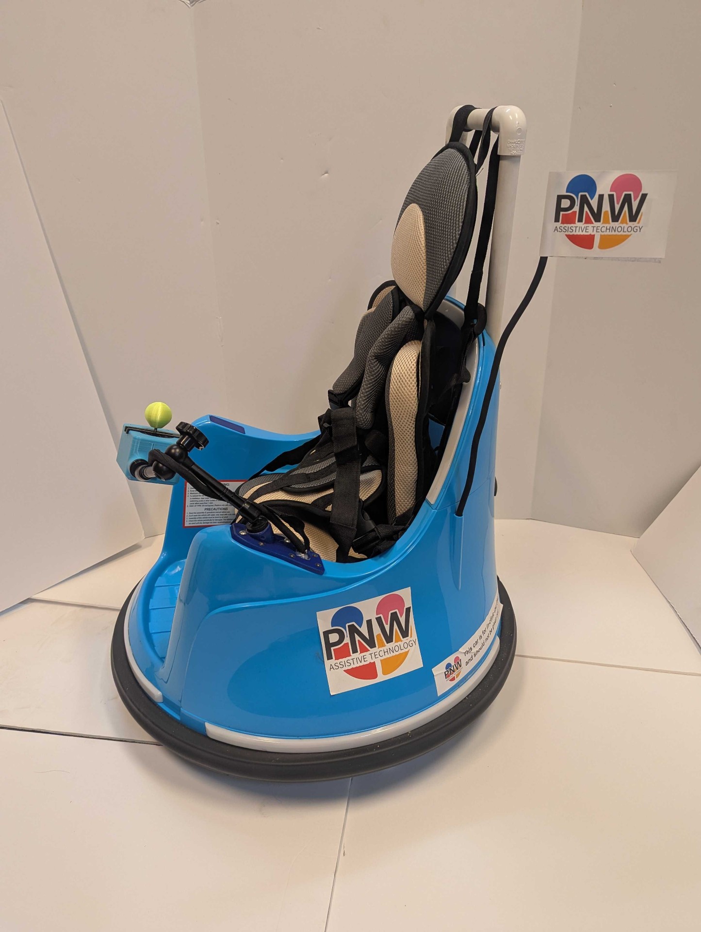 The Littlest Wayfinder™ — a bright blue adapted ride-on with a five-point harness, head support, and adaptive switch.