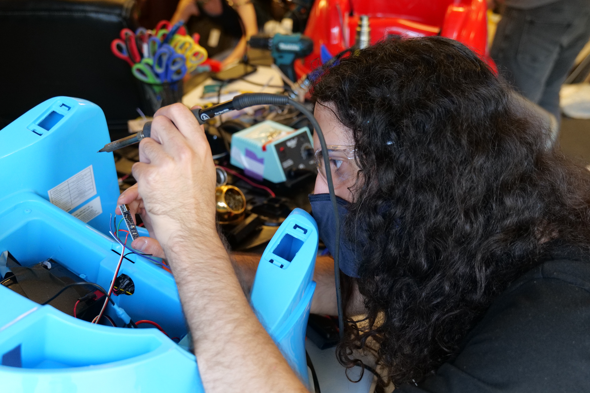 A masked volunteer carefully solders a custom control board inside a blue Wayfinder™ build.