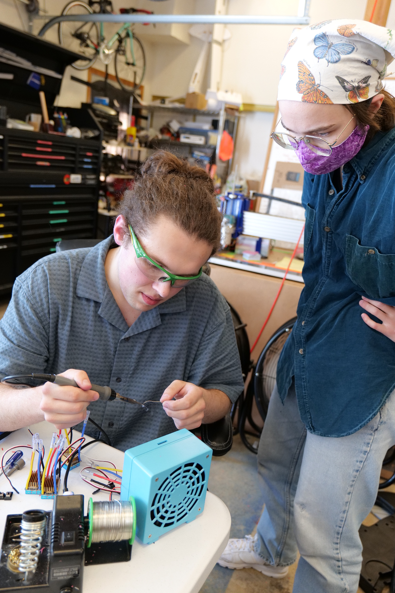 Two PNW Assistive Technology volunteers soldering wires together at the build bench.